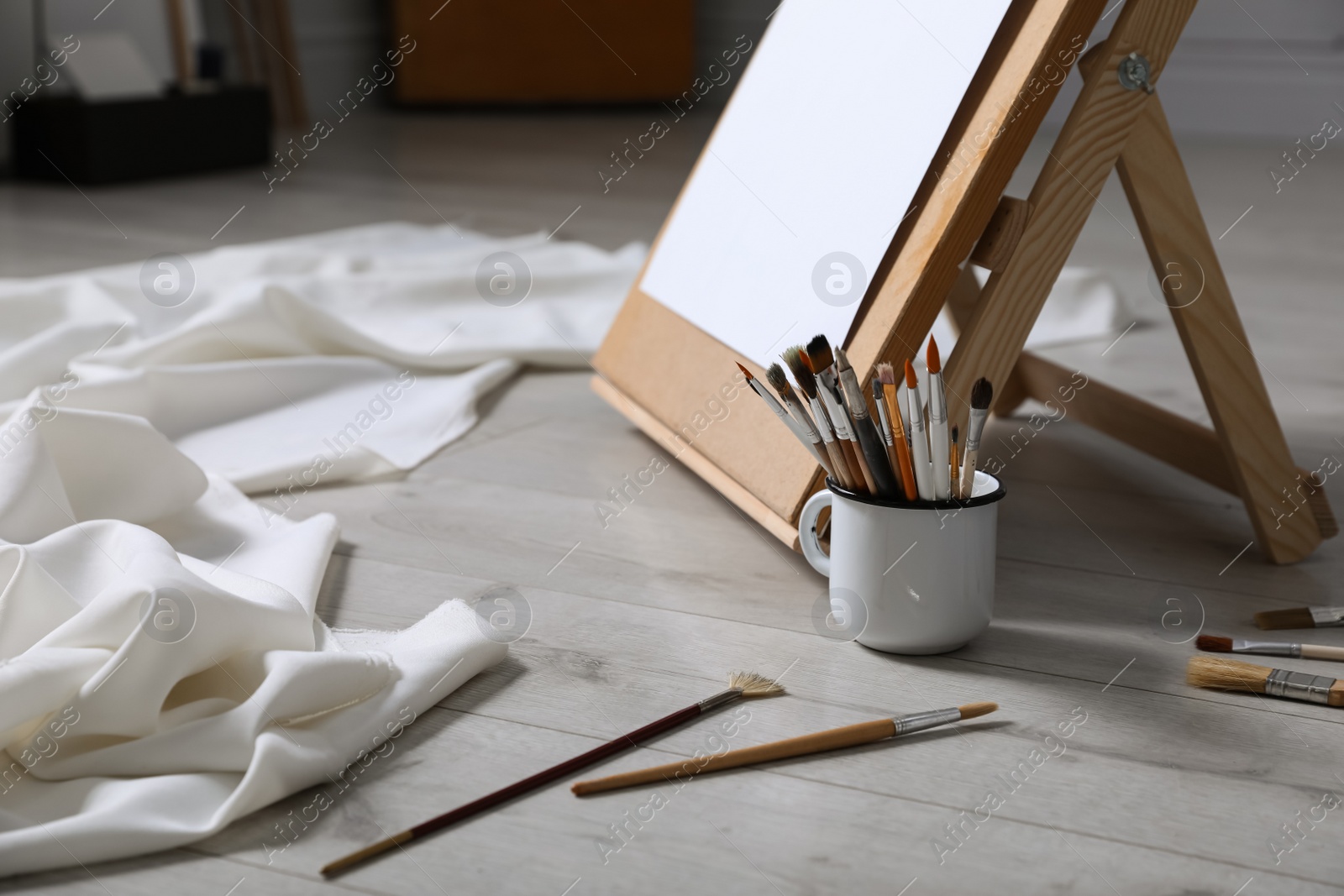 Photo of Different brushes near stand with canvas on floor in artist's studio, space for text