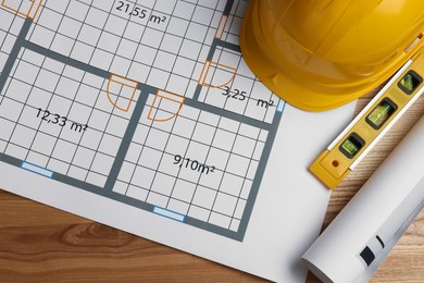 Photo of Construction drawings, safety hat and bubble level on wooden table