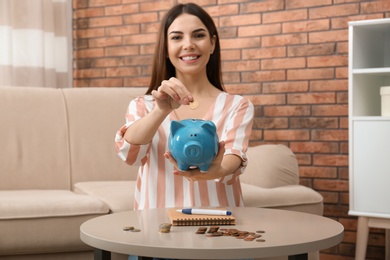 Happy young woman with piggy bank and money at home