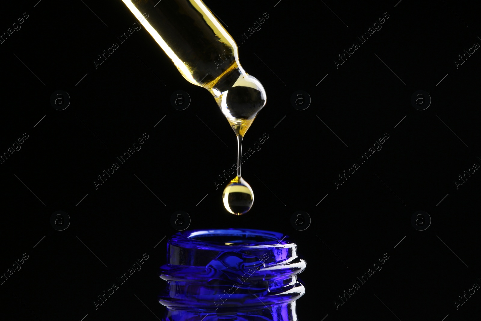 Photo of Dripping tincture from pipette into bottle on black background, closeup