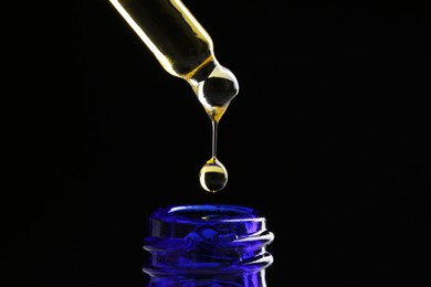 Photo of Dripping tincture from pipette into bottle on black background, closeup