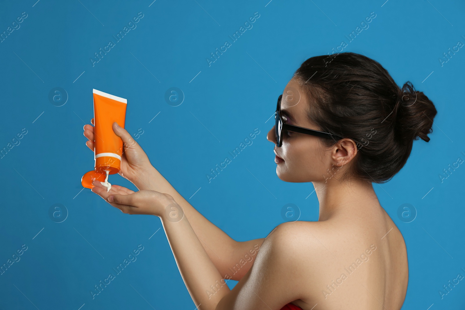 Photo of Young woman applying sun protection cream on dark blue background