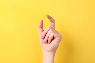Photo of Woman holding vitamin capsule on yellow background, closeup