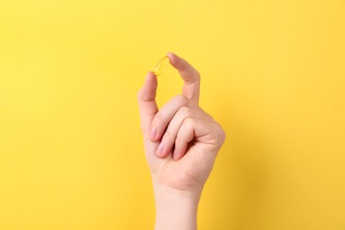 Woman holding vitamin capsule on yellow background, closeup