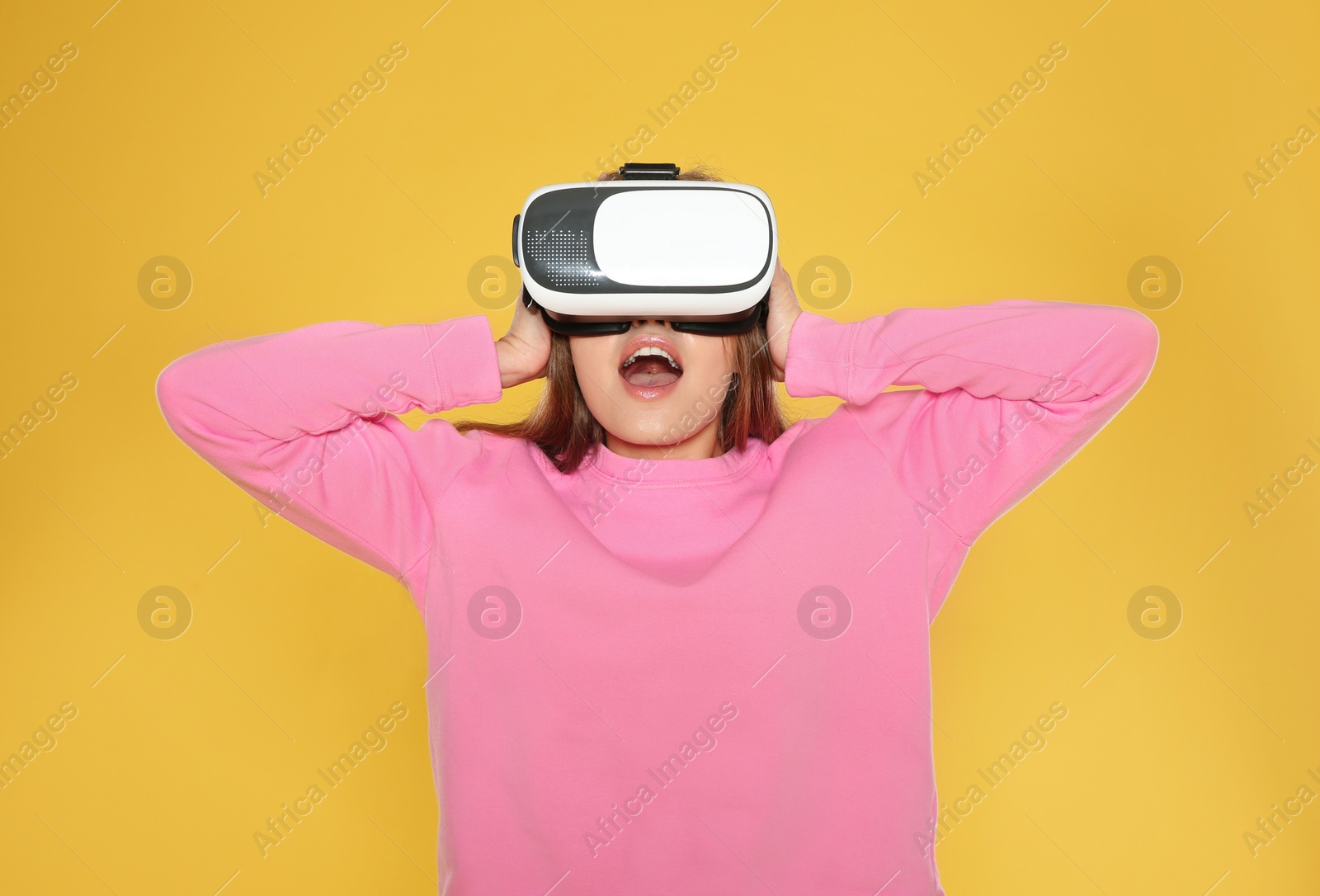 Photo of Emotional young woman playing video games with virtual reality headset on color background