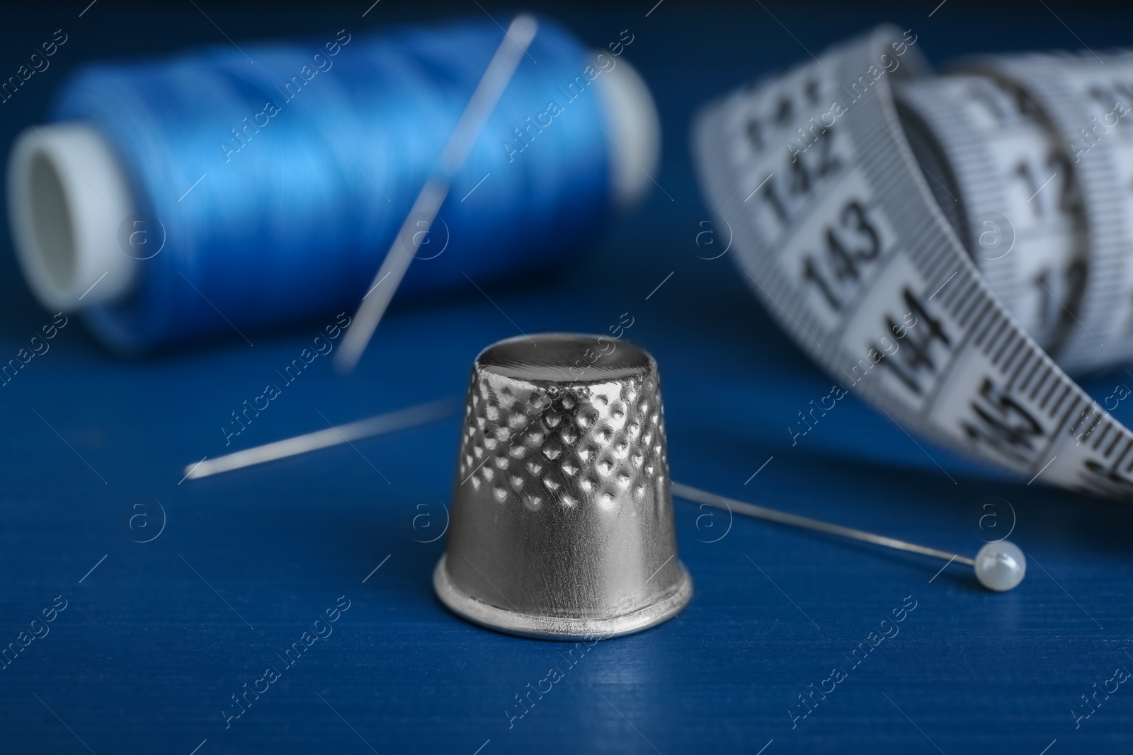 Photo of Silver thimble on blue wooden table. Sewing accessories