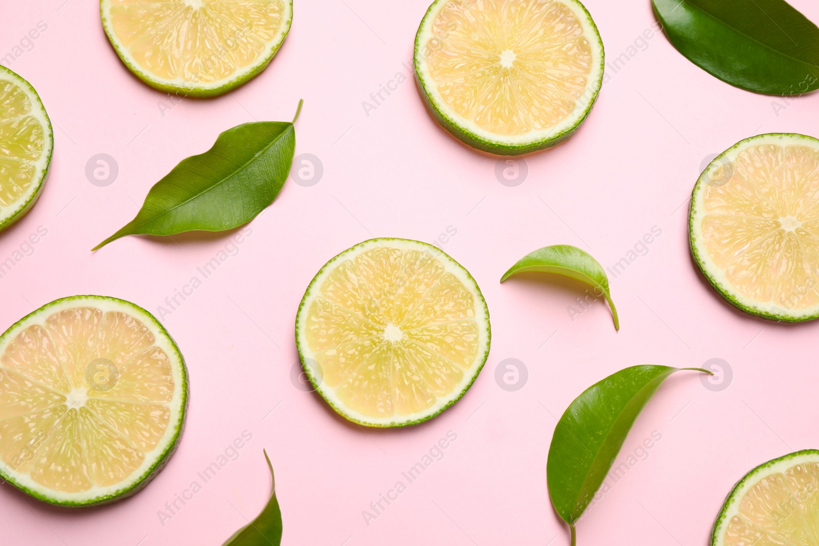 Photo of Juicy fresh lime slices and green leaves on pink background, flat lay