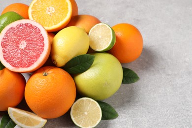 Pile of different fresh citrus fruits and leaves on grey textured table, closeup. Space for text