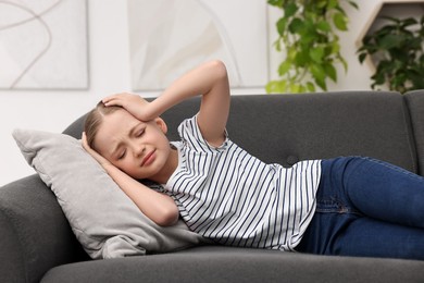 Photo of Little girl suffering from headache on sofa indoors