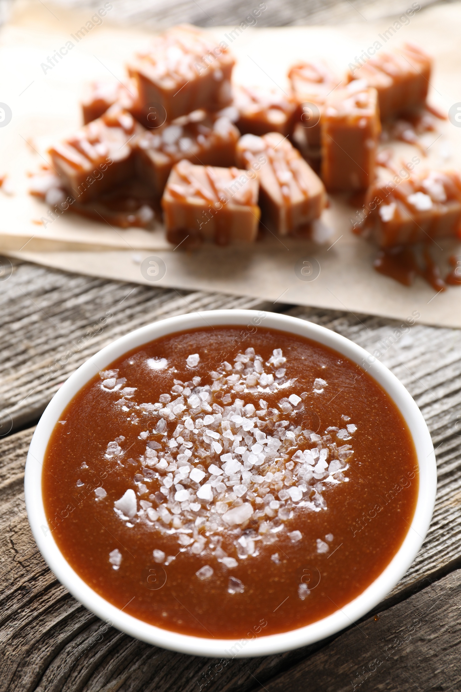 Photo of Caramel sauce with sea salt in bowl on wooden table, closeup