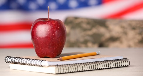 Image of Military education. Notebooks, apple and pencil on table against flag of USA