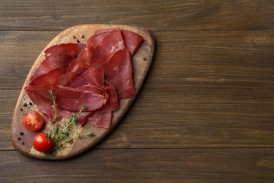 Photo of Tasty bresaola, peppercorns, tomatoes and thyme on wooden table, top view. Space for text