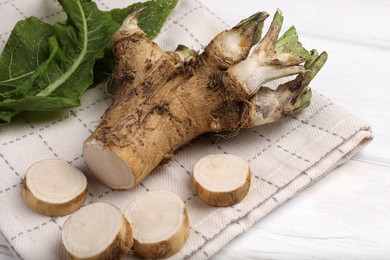 Photo of Cut horseradish root and leaves on white wooden table, closeup