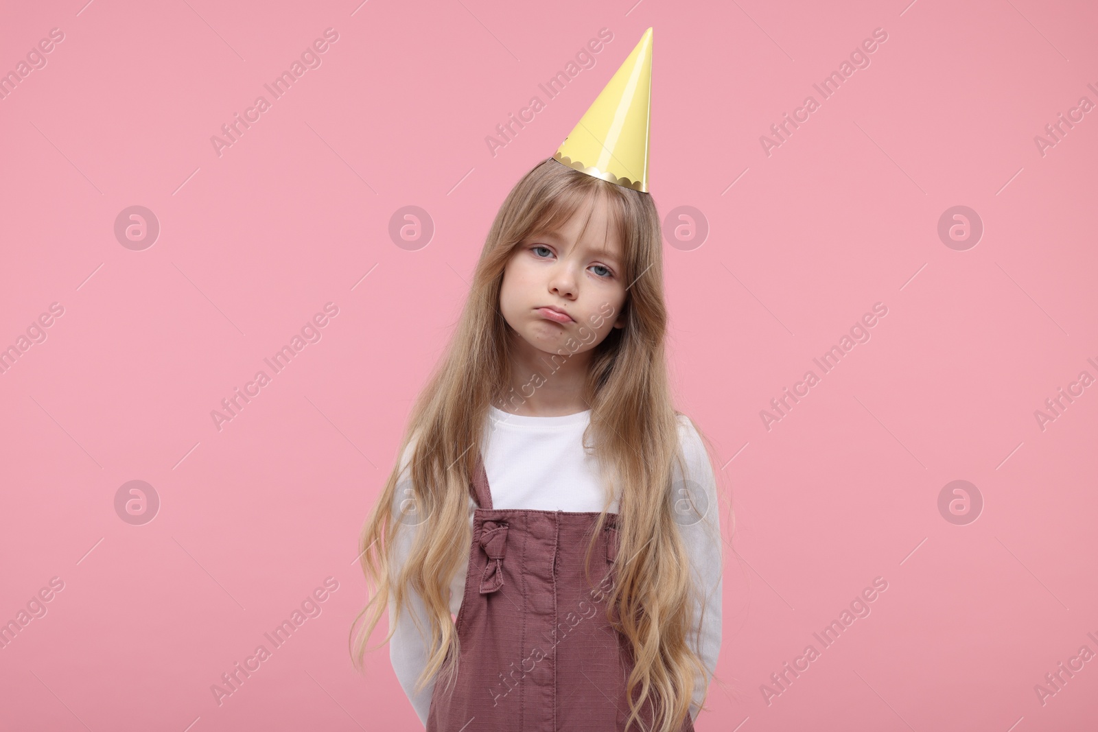 Photo of Bored little girl in party hat on pink background