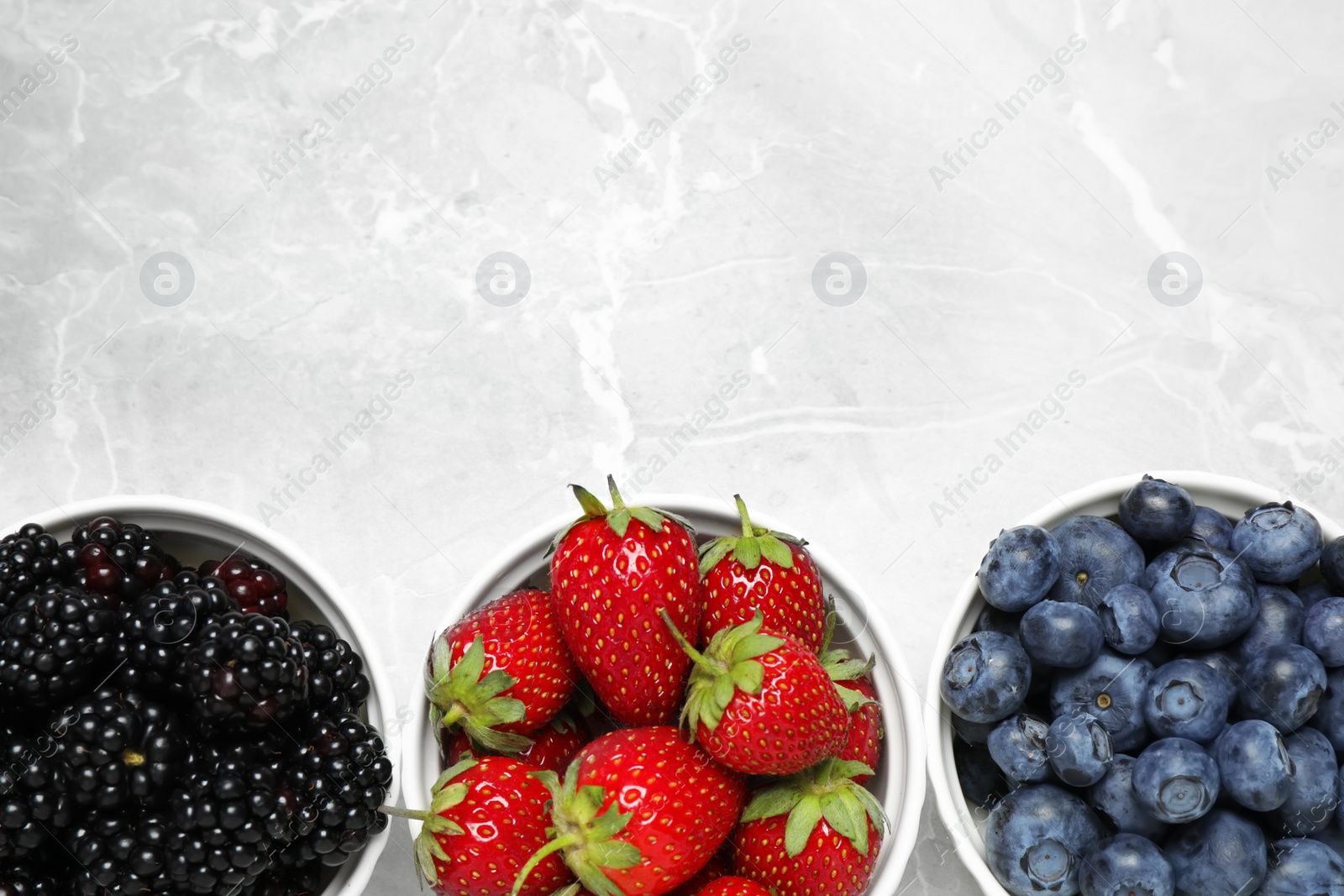 Photo of Different ripe berries on light marble table, flat lay. Space for text