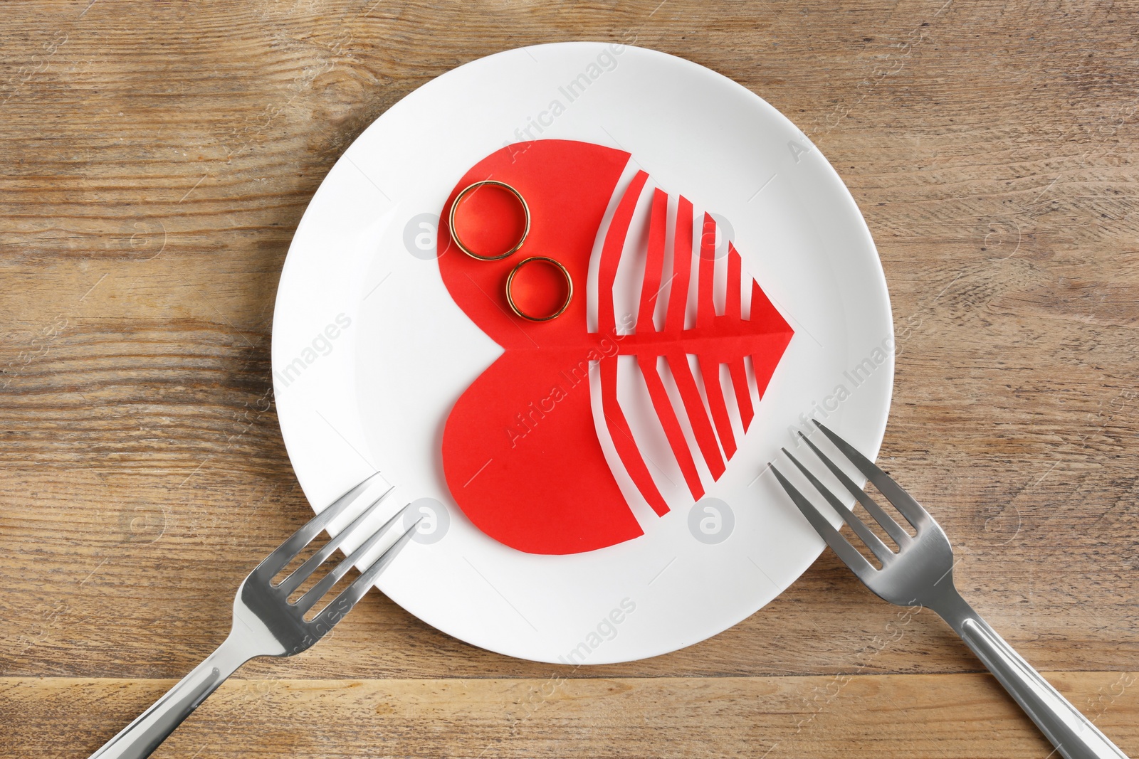 Photo of Divorce concept. Plate with paper cutout of heart, wedding rings and forks on wooden table, flat lay