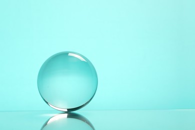 Photo of Transparent glass ball on turquoise background. Space for text