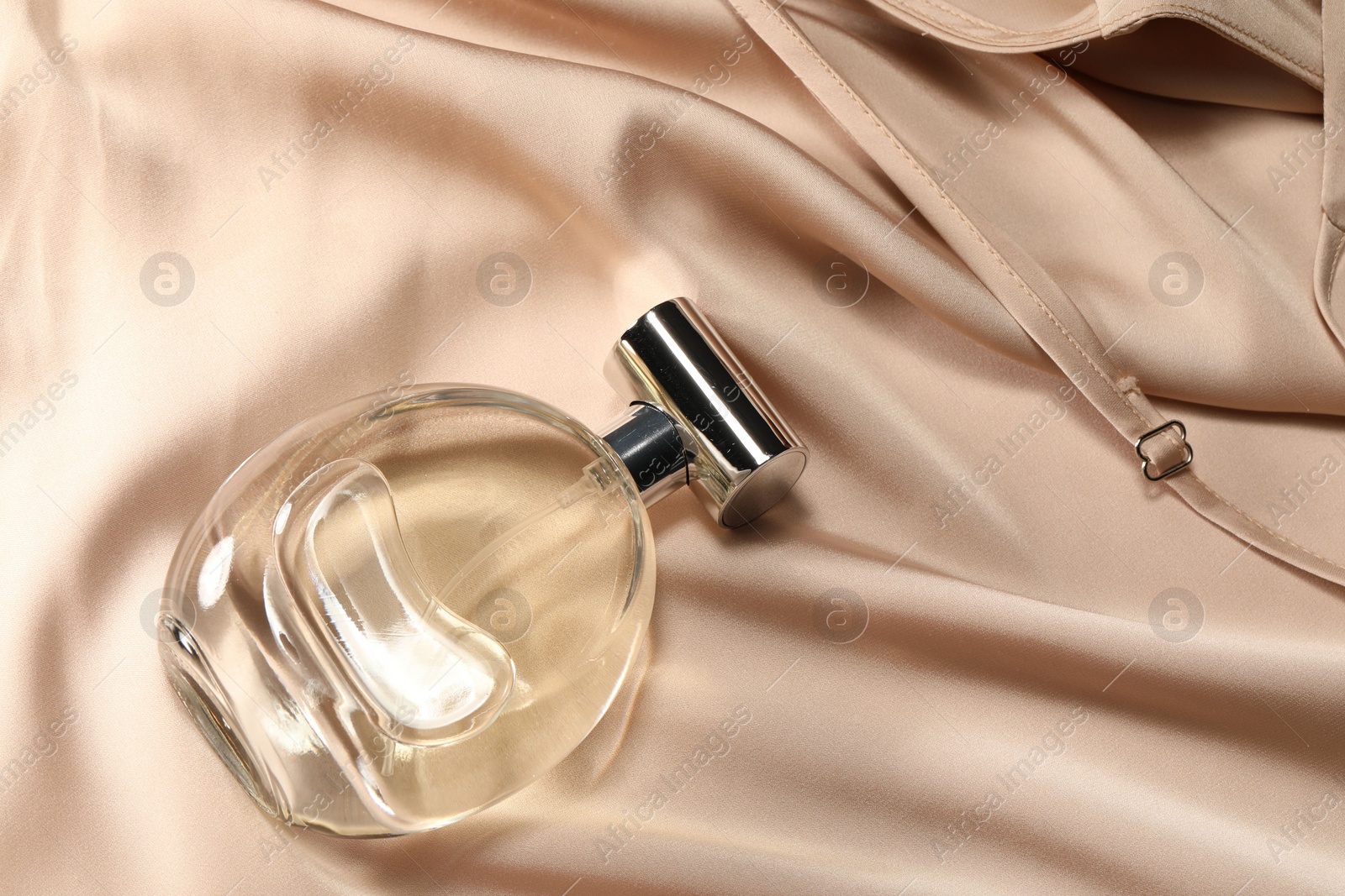 Photo of Luxury perfume in bottle on beige silk fabric, top view