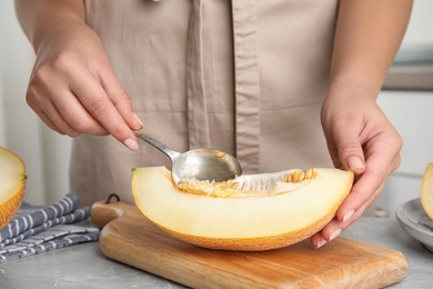 Young woman removing seeds from ripe melon with spoon at grey marble table, closeup