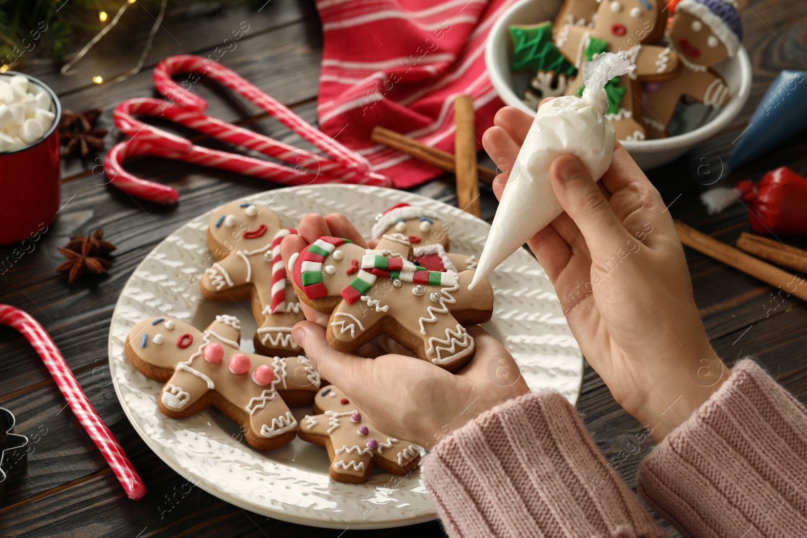 Photo of Making homemade Christmas cookies. Girl decorating gingerbread man at wooden table, closeup