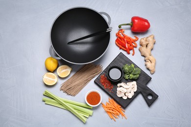 Photo of Wok, chopsticks and different products on grey table, flat lay