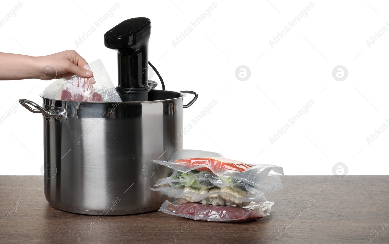 Photo of Woman putting vacuum packed meat into pot with sous vide cooker on wooden table against white background, closeup. Thermal immersion circulator