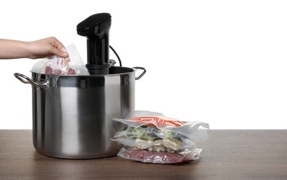 Photo of Woman putting vacuum packed meat into pot with sous vide cooker on wooden table against white background, closeup. Thermal immersion circulator