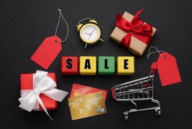 Photo of Wooden cubes with word Sale, gift boxes, shopping cart, credit cards and alarm clock on color background, flat lay