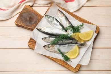 Photo of Fresh raw sprats, lemon and dill on light wooden table, top view