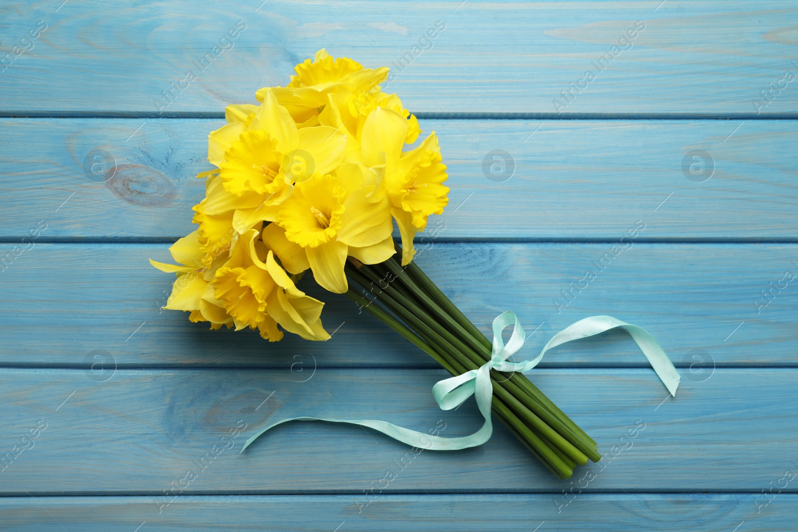 Photo of Beautiful daffodil bouquet on blue wooden table, top view