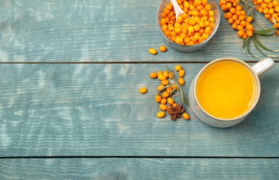 Photo of Sea buckthorn tea and fresh berries on blue wooden table, flat lay. Space for text