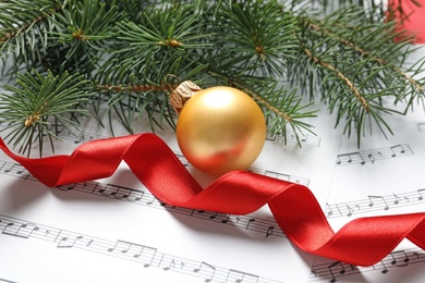Photo of Fir tree branches with Christmas ball and ribbon on music sheets