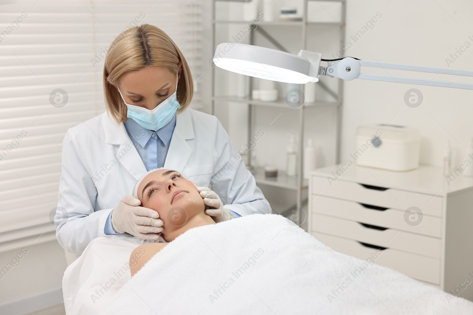 Photo of Dermatologist examining patient`s face under lamp in clinic