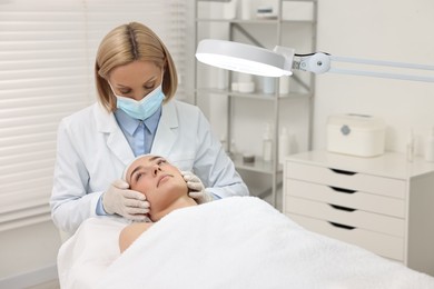 Dermatologist examining patient`s face under lamp in clinic