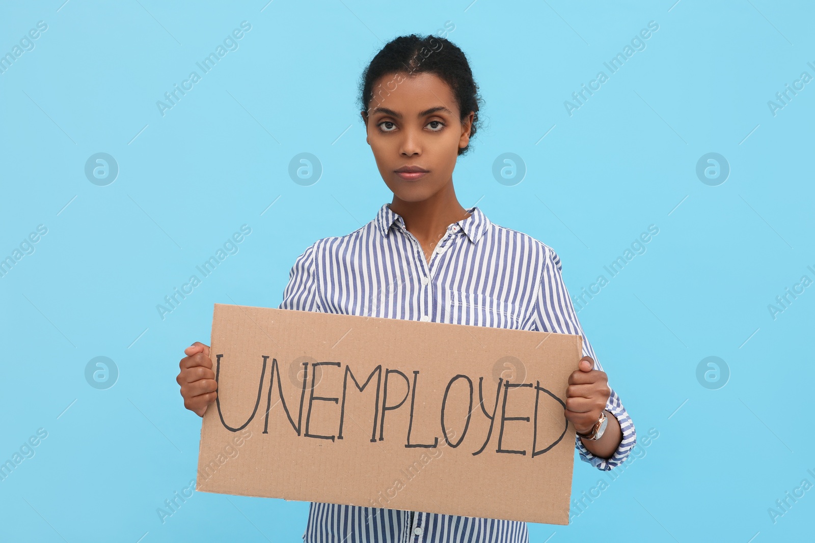 Photo of African American woman holding sign with word Unemployed on light blue background