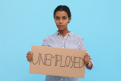 Photo of African American woman holding sign with word Unemployed on light blue background