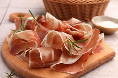 Slices of tasty cured ham and rosemary on tiled table, closeup