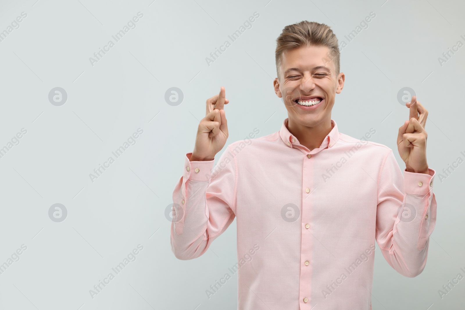 Photo of Happy young man crossing his fingers on light grey background. Space for text