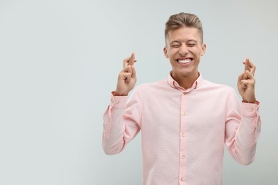 Photo of Happy young man crossing his fingers on light grey background. Space for text