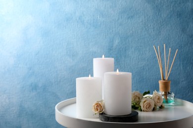 Photo of Burning candles, air reed diffuser and beautiful roses on white table near light blue wall, space for text