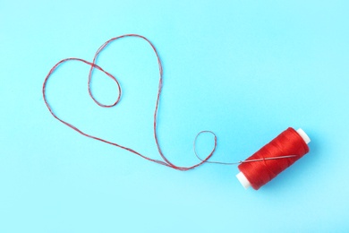 Heart made of red thread on color background, top view