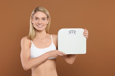 Slim woman holding scales on brown background. Weight loss