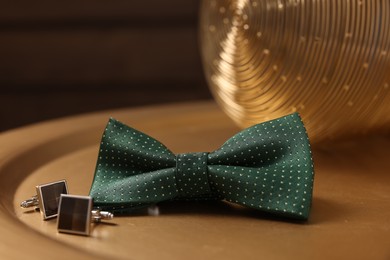 Photo of Stylish green bow tie and cufflinks on golden table, closeup