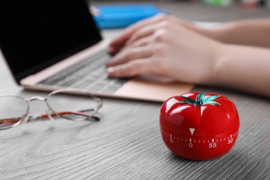 Photo of Woman working on laptop at wooden table, focus on kitchen timer in shape of tomato. Space for text