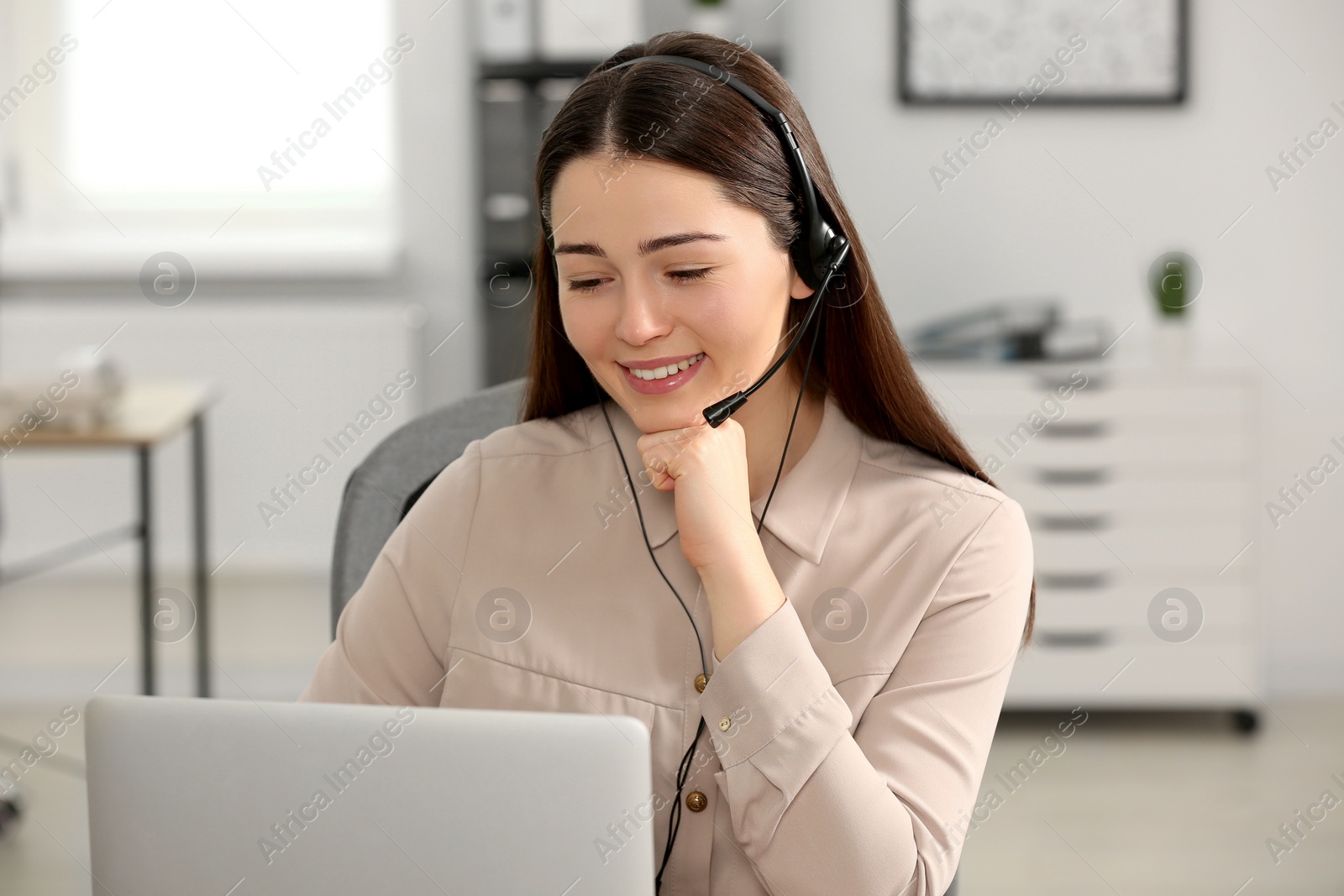 Photo of Hotline operator with headset working on laptop in office