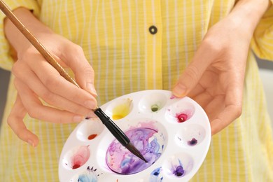 Woman mixing watercolor paints in art palette, closeup