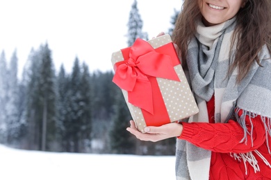 Happy woman with gift box outdoors, space for text. Winter vacation