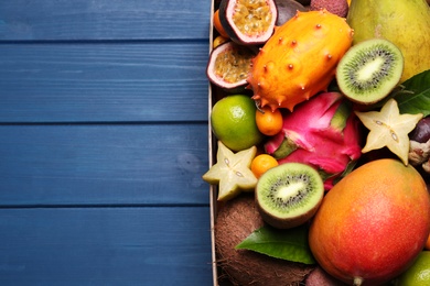 Crate with different exotic fruits on blue wooden table, top view. Space for text