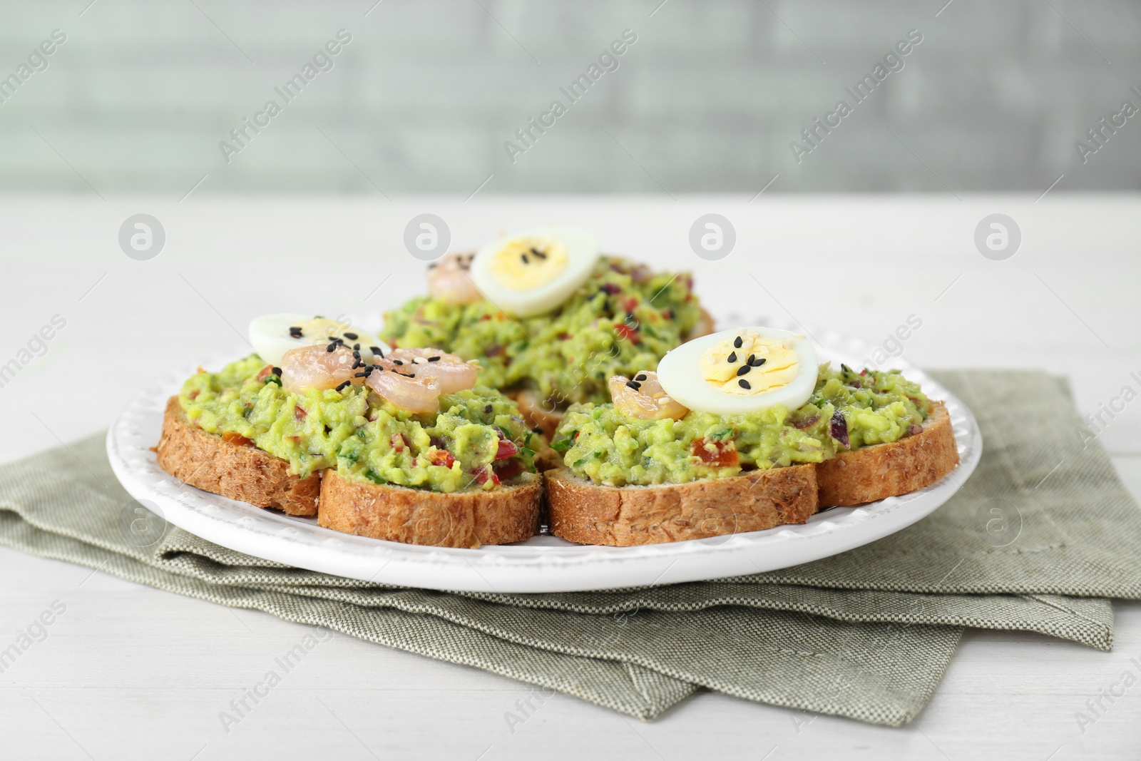 Photo of Slices of bread with tasty guacamole, eggs and shrimp on white wooden table, closeup