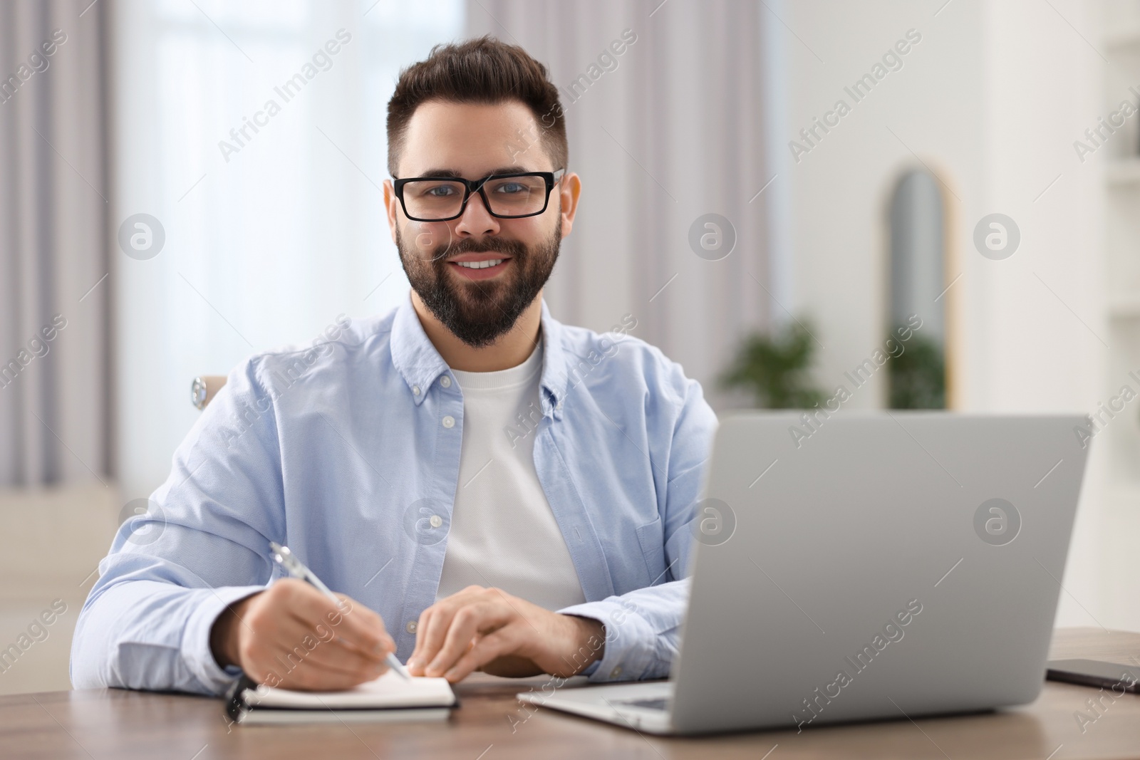 Photo of Young man in glasses watching webinar at table in room